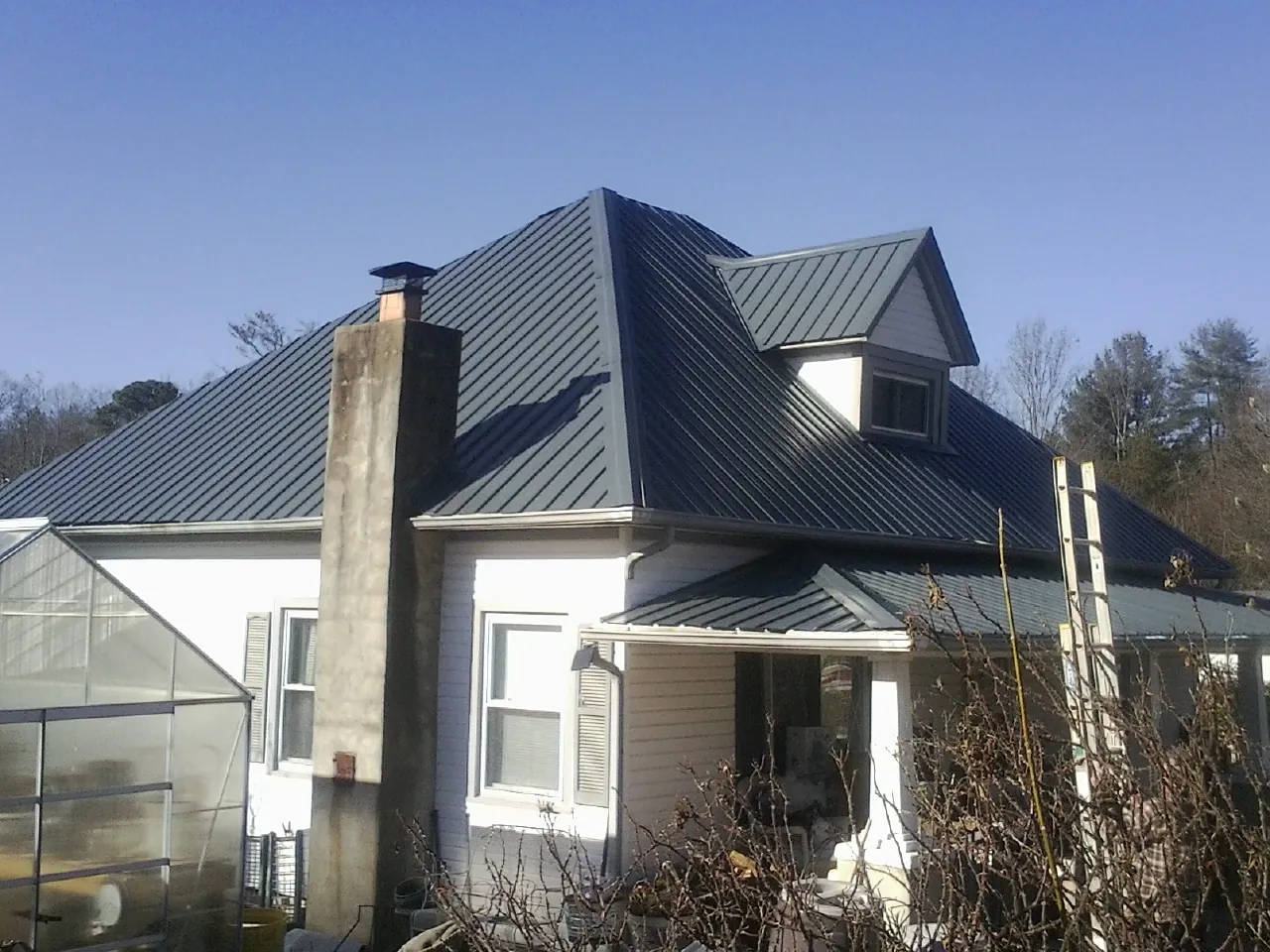 Dark blue standing seam metal roof on a white farmhouse with dormer — Slate & Tile Roof Repair by Roofing Brothers in Fennville