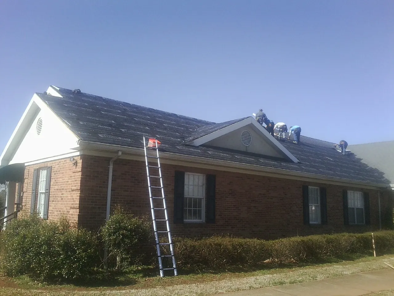 Crew tearing shingles off a brick ranch roof with a ladder set — Emergency Roof Repair work by our crew in Fennville
