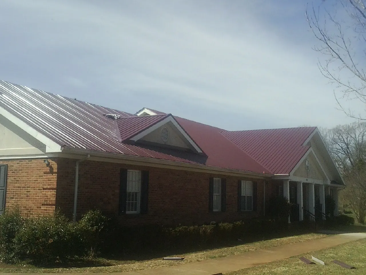 Red metal roof with gabled entries on a long brick building, from a Hail Damage Roof Repair job in Fennville