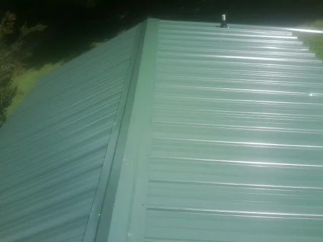 New green metal panels meeting at the ridge of a roof — Flat Roof Repair work by our crew in Fennville