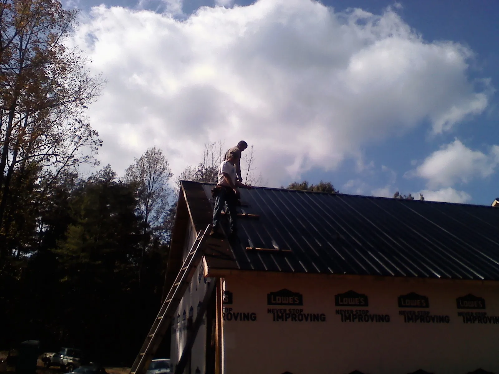 Roofer fastening dark metal panels high against a cloudy sky, from a Roof Inspection job in Fennville