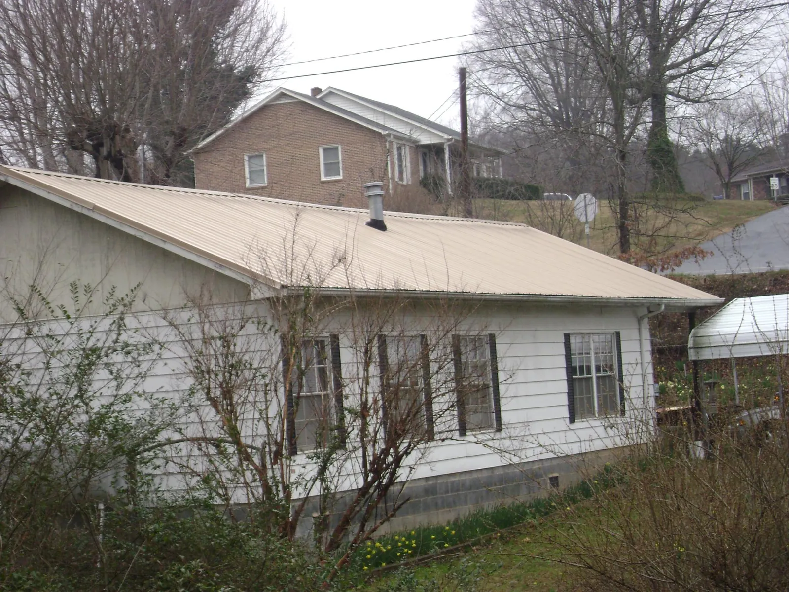 Tan metal roof on a white sided house set into a hillside — Commercial Roofing by Roofing Brothers in Fennville